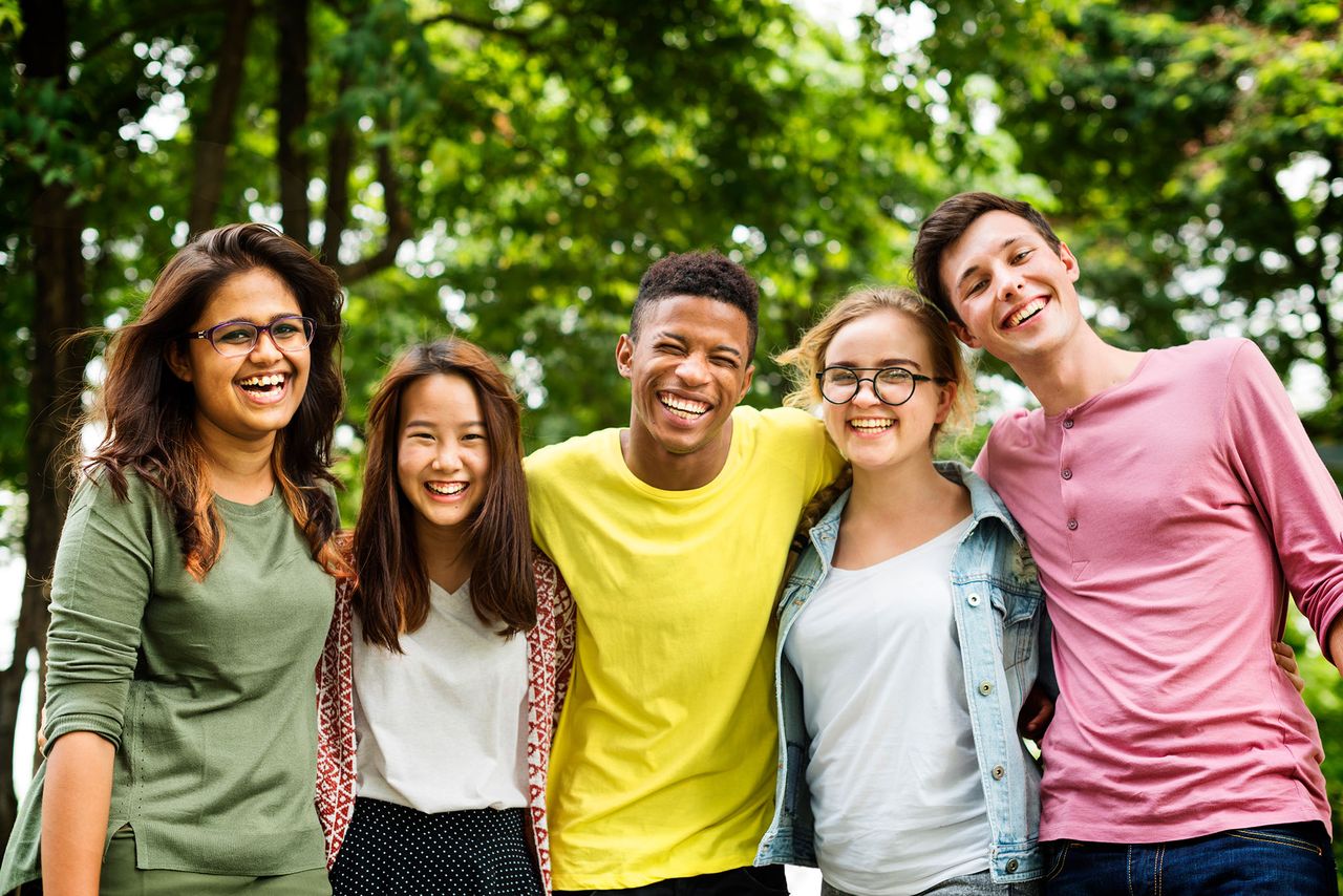 A group of smiling young people standing arm in arm outdoors